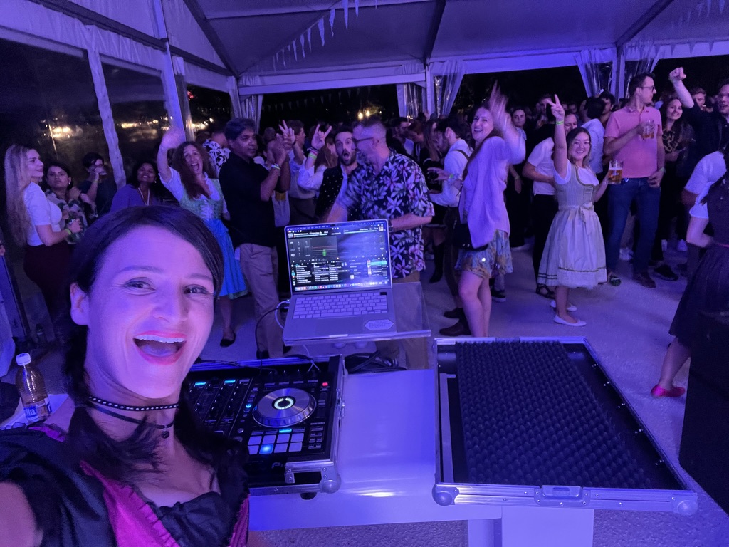 Ein lächelnder DJ macht ein Selfie auf einer lebhaften Party in Zürich, während die Leute im Hintergrund tanzen und feiern.