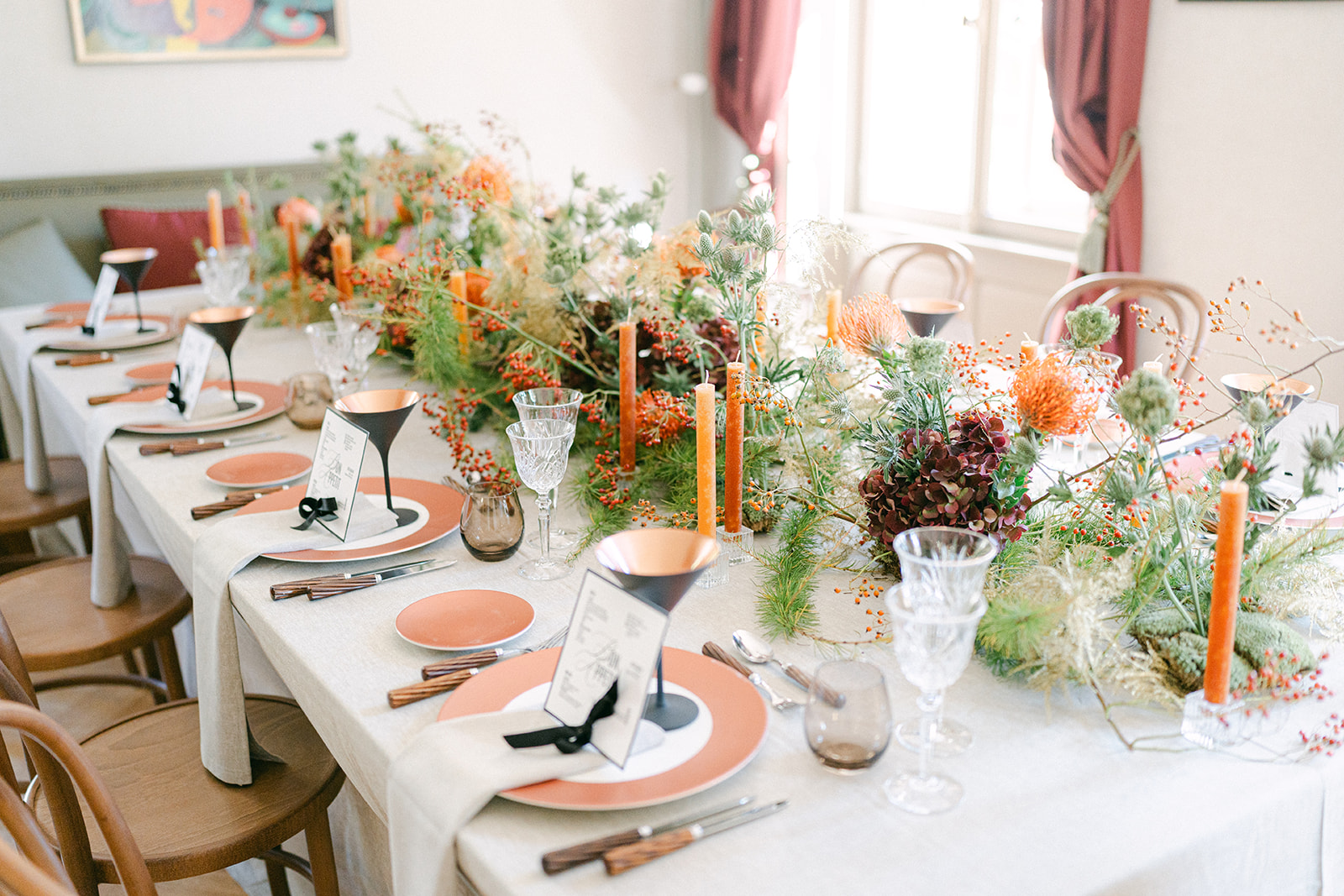 Elegant gedeckter Tisch mit orangefarbenen Kerzen, floralem Tafelaufsatz, Gläsern und Speisekarten auf pfirsichfarbenen Tellern - perfekt für eine stilvolle Hochzeit in Zürich oder irgendwo in der Schweiz.