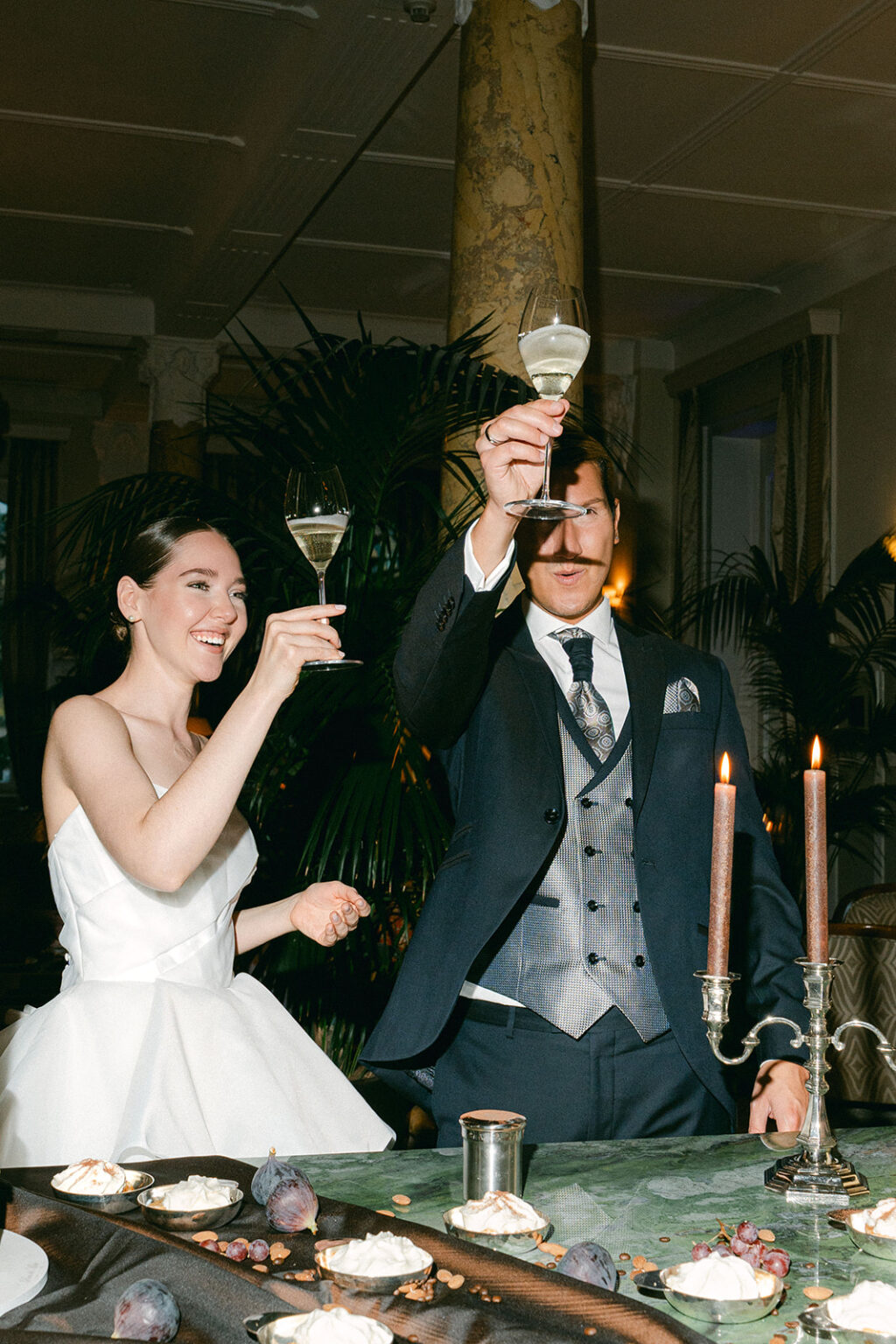 A formally dressed wedding couple clinks glasses at a beautifully decorated table, ready to dance the night away with their wedding DJ in Switzerland.