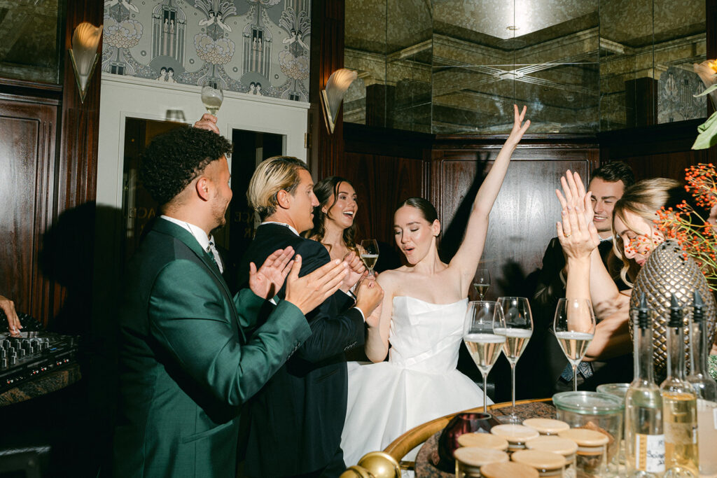 Eine Gruppe formell gekleideter Menschen feiert und jubelt mit Getränken auf einer Hochzeit in Zürich, eine Frau - vielleicht die Traurednerin - hebt freudig ihren Arm im Herzen der Schweiz.