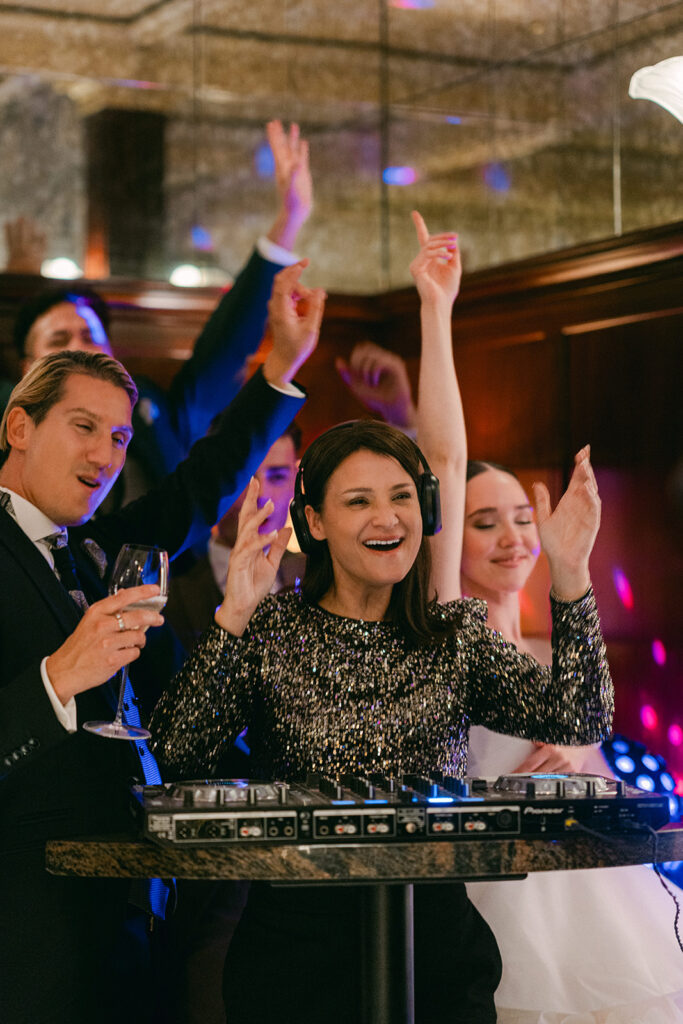 A wedding DJ in sparkling dresses plays music while people dance and celebrate with a wedding officiant at a festive indoor event in Zurich.