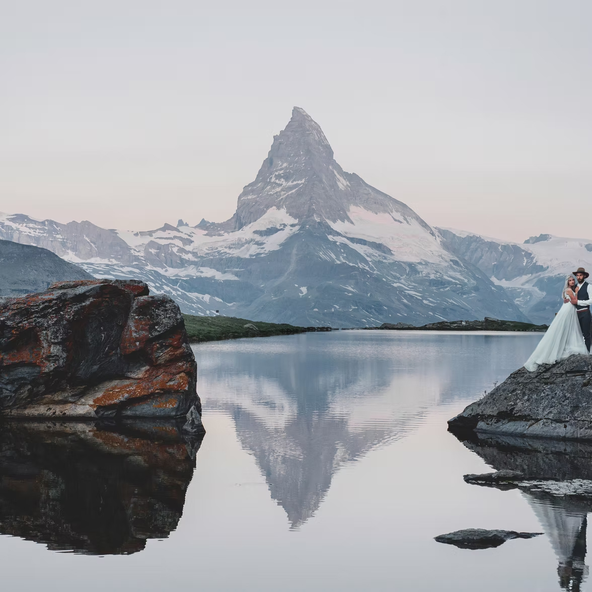 Braut und Bräutigam umarmen sich an einem See in der Nähe von Zürich. Das Matterhorn spiegelt sich im Wasser, während eine Hochzeitssängerin ihrem besonderen Tag eine magische Note verleiht.